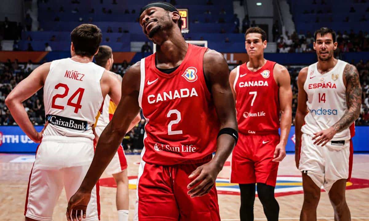 A Canadian basketball player wearing jersey number 2 looks frustrated, standing among teammates and opponents from Spain during a game. Other players are visible in the background on the court.